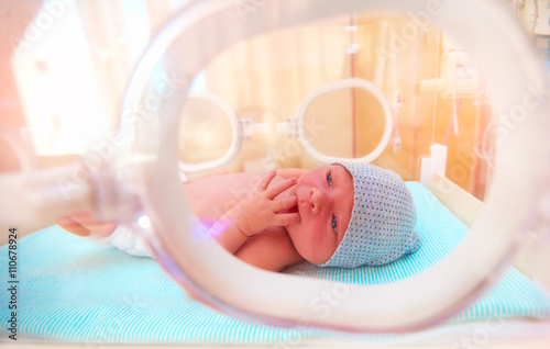 newborn baby lying inside the infant incubator in hospital, sucking fingers