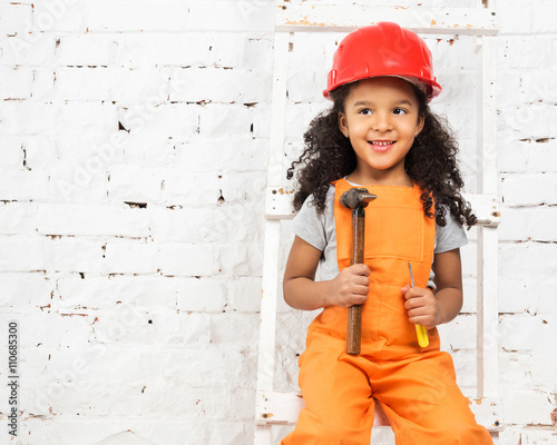 smiling little girl in helmet with hammer and screwdriver sitting on ladder © Ievgen Skrypko