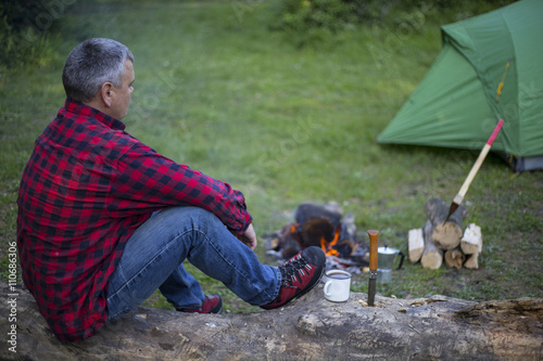 Man prepares coffee on a fire in a tent camp.