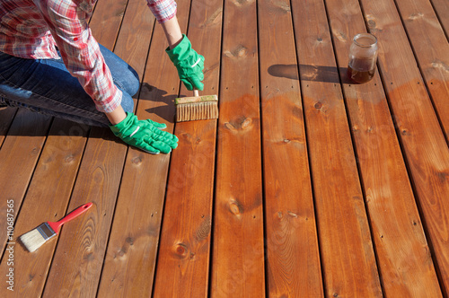 Photography Woman applying protective varnish or wood oil on a patio wooden floor, house maintenance concept