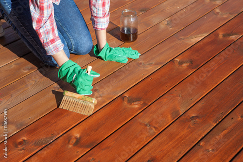 Canvas Print Woman applying protective varnish or wood oil on a patio wooden floor, house maintenance concept
