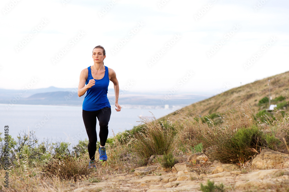 Woman running up hill with sea in background