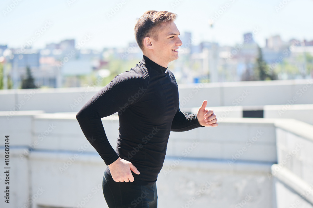 Athlete in black tight clothes runs on the background of the city and smiling Athlete in black tight clothes runs on the background of the city and smiling