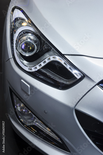 Сar headlight, hood and bumper with plastic air intake of powerful sports car with silver metallic glossy bodywork 