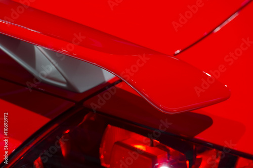 Curved spoiler of aggressive powerful sport car with red bodywork, selective focus 