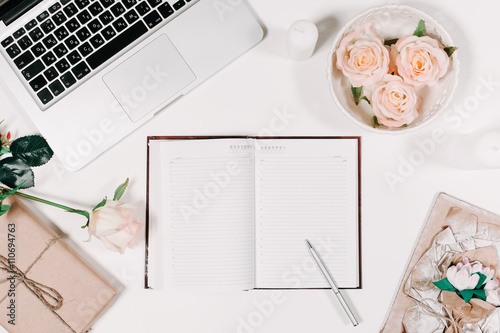 Workspace with diary, pen, vintage white tray, pink rose, gift in parchment on white background. Top view, flat lay