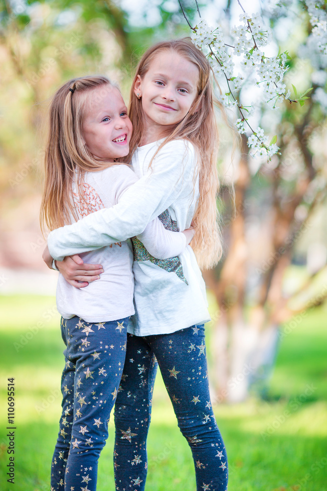 Adorable little girls in blooming cherry tree garden on spring day