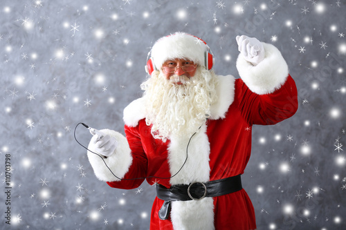 Santa Claus with headphones listening to music on gray wall background with snow effect