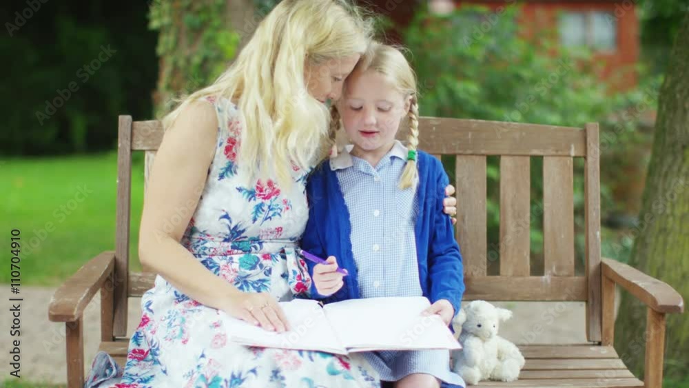  Affectionate mother and daughter sitting in garden together doing homework