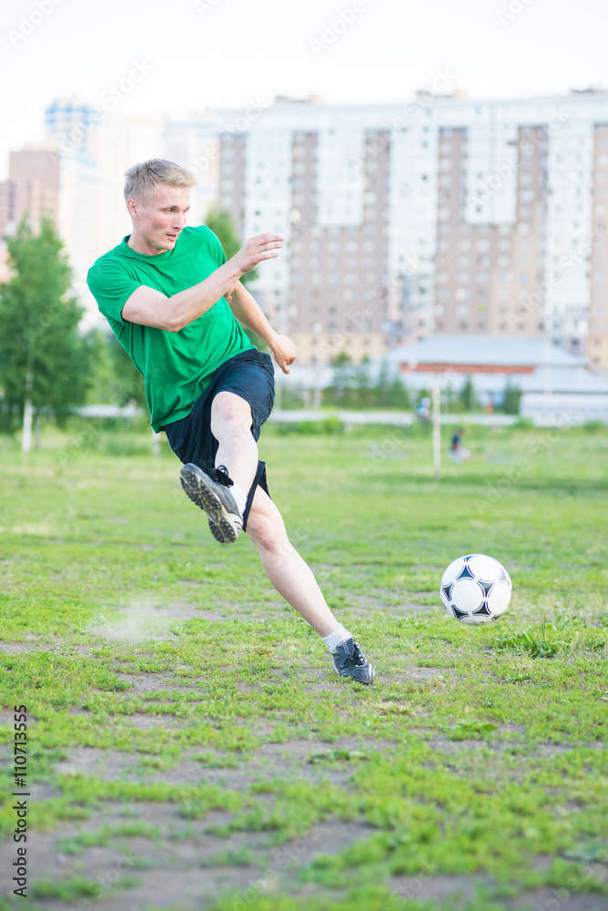 Soccer player strongly hits the ball. City park playground.