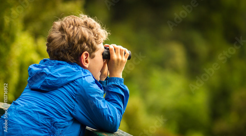 young boy bird watching in a forest photo