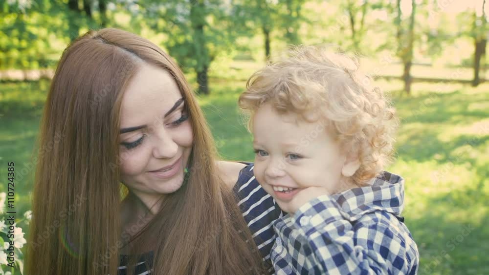 Young beautiful mum holds on hands of his son's curly. They walk on a spring park and enjoy. Young beautiful mum holds on hands of his son's curly. They walk on a spring park and enjoy.