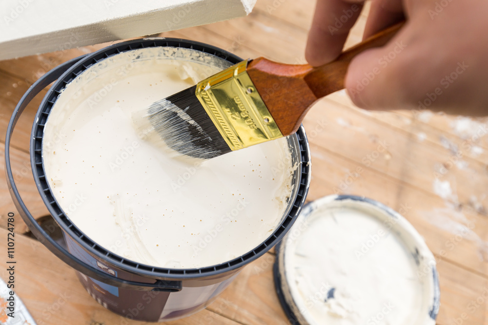 Holding painting brush in the jar with the white paint. Painting timber boards outside with the white paint or white coloured emulsion using 2 inches painting brush.