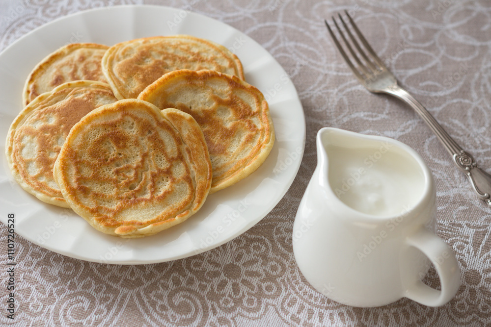 Freshly baked pancakes with sour cream on a textile tablecloths Freshly baked pancakes with sour cream on a textile tablecloths