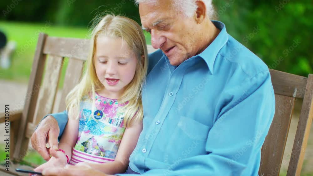 Grandfather & granddaughter sitting in the garden, looking at tablet computer Grandfather & granddaughter sitting in the garden, looking at tablet computer
