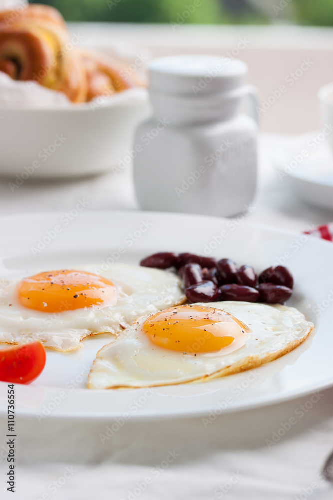 Homemade fried eggs with tomatoes and red kidney beans on a plate on a table with kitchen background, closeup Homemade fried eggs with tomatoes and red kidney beans on a plate on a table with kitchen background, closeup