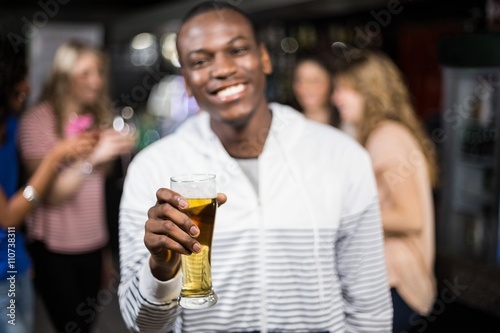 Canvastavla Smiling man showing a beer with his friends