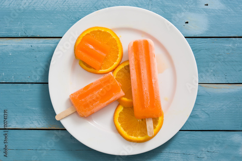 Fototapeta Naklejka Na Ścianę i Meble -  Orange popsicles on blue wooden background
