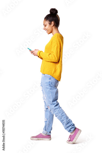 Smiling young woman walking and looking at mobile phone
