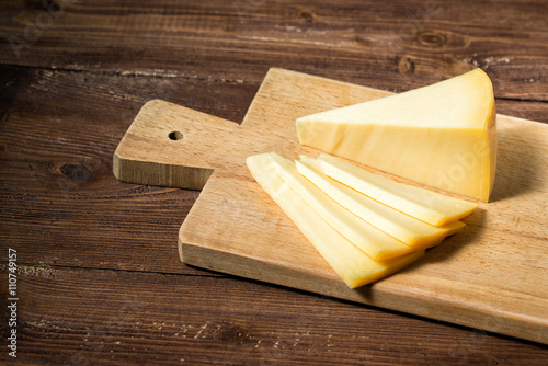 Cheese sliced on a cutting board, wooden background