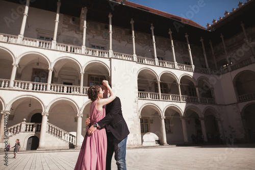 Beautiful couple, man, girl with long pink dress posing in old castle near columns. Krakow Vavel