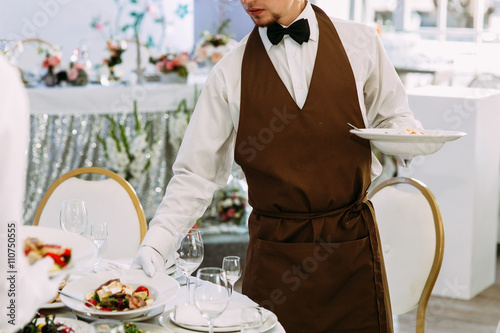 Wedding waiter is serving a table with meals
