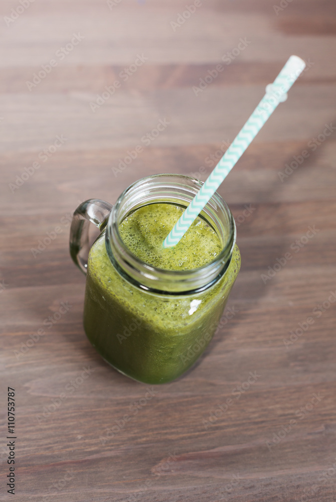 A green smoothee in a mason jar with tube on wooden background A green smoothee in a mason jar with tube on wooden background