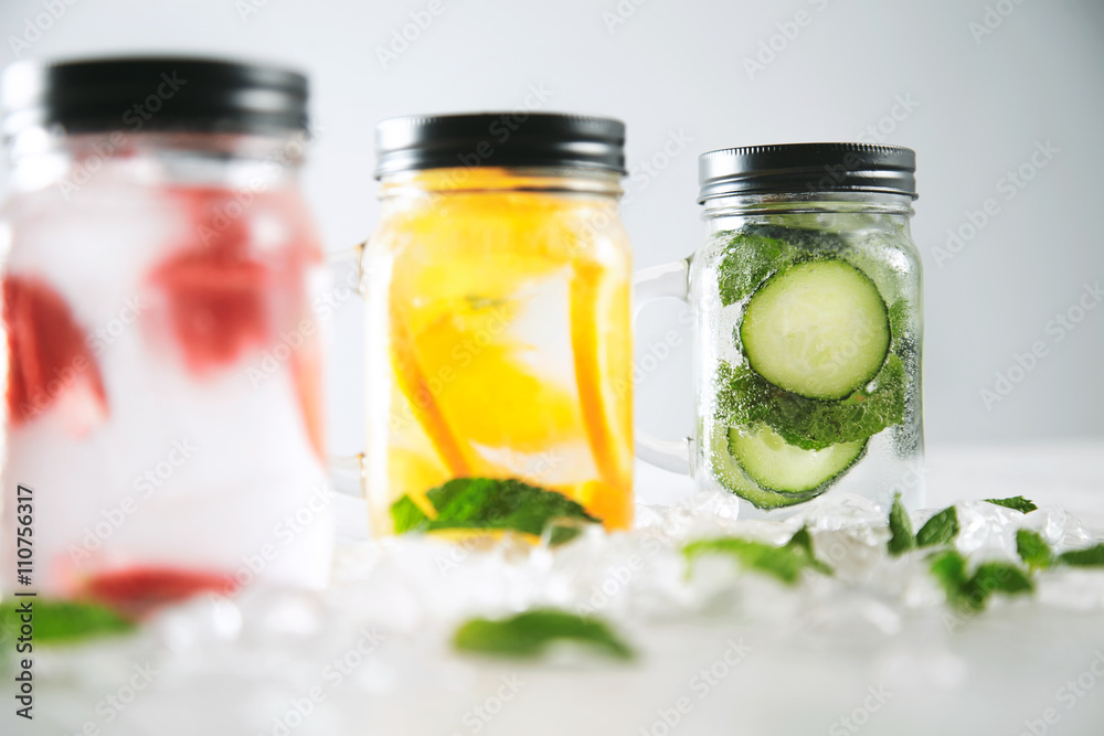 Close focus on last jar Healthy fresh cool homemade lemonades with sparkling water strawberry, cucumber,mint and orange isolated in smashed ice cubes on wooden table Close focus on last jar Healthy fresh cool homemade lemonades with sparkling water strawberry, cucumber,mint and orange isolated in smashed ice cubes on wooden table