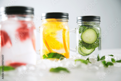 Close focus on last jar Healthy fresh cool homemade lemonades with sparkling water strawberry, cucumber,mint and orange isolated in smashed ice cubes on wooden table