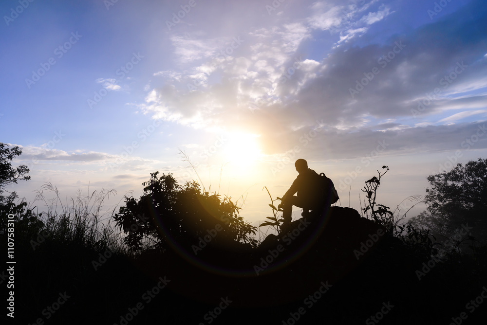 Silhouette man sitting on mountain peak at sunrise.