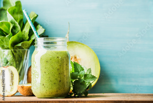 Freshly blended green fruit smoothie in glass jar with straw
