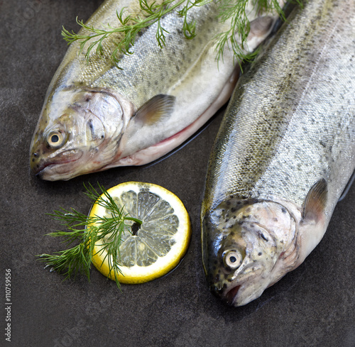 Raw rainbow trouts on a stone board, with herbs and lemon, ready for cooking