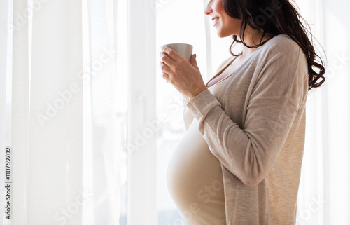 close up of pregnant woman with tea cup at window