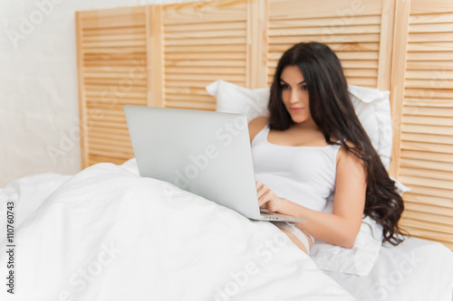 Smiling woman lying on bed with her laptop