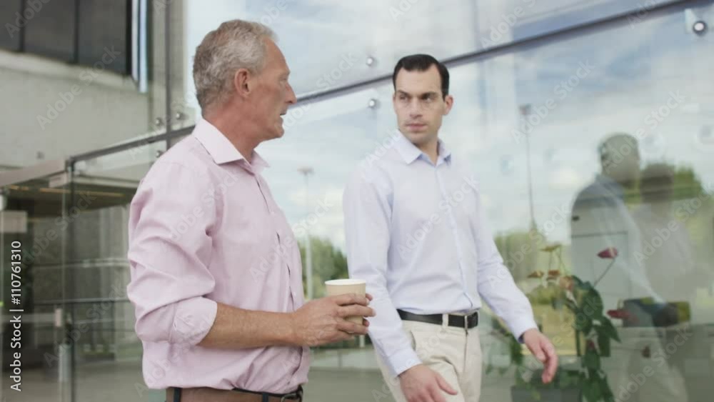 2 Businessmen in conversation as they walk outside office building 2 Businessmen in conversation as they walk outside office building