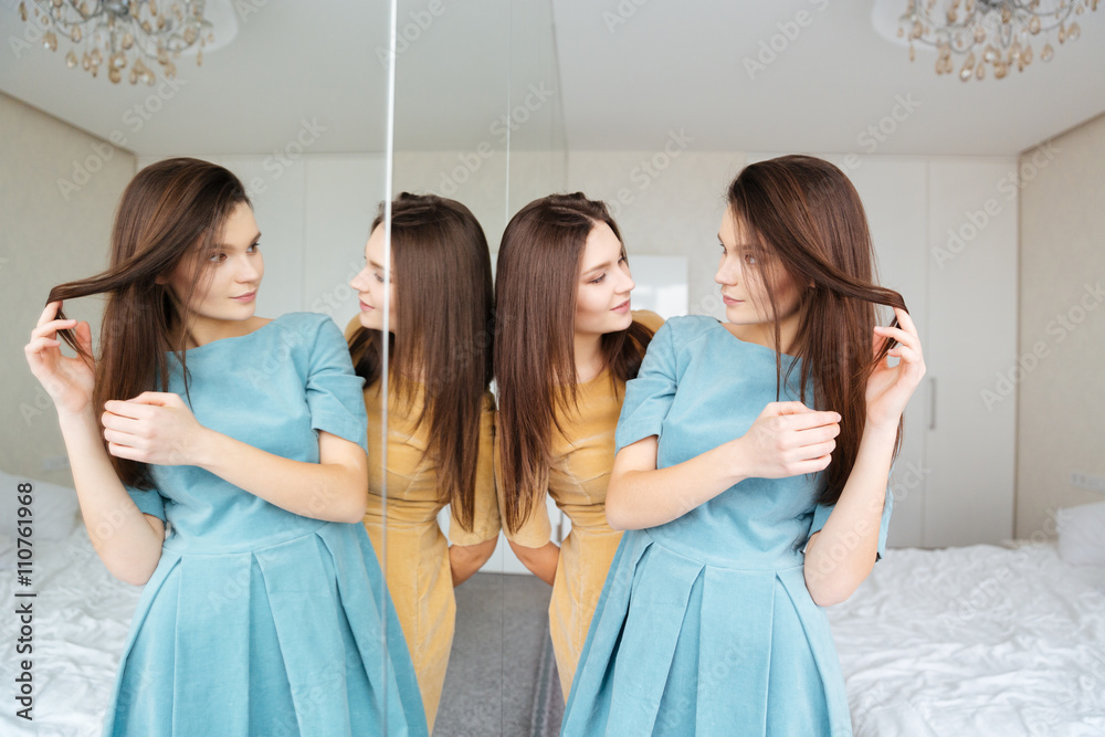 Two sisters twins standing and looking at the mirror Two sisters twins standing and looking at the mirror