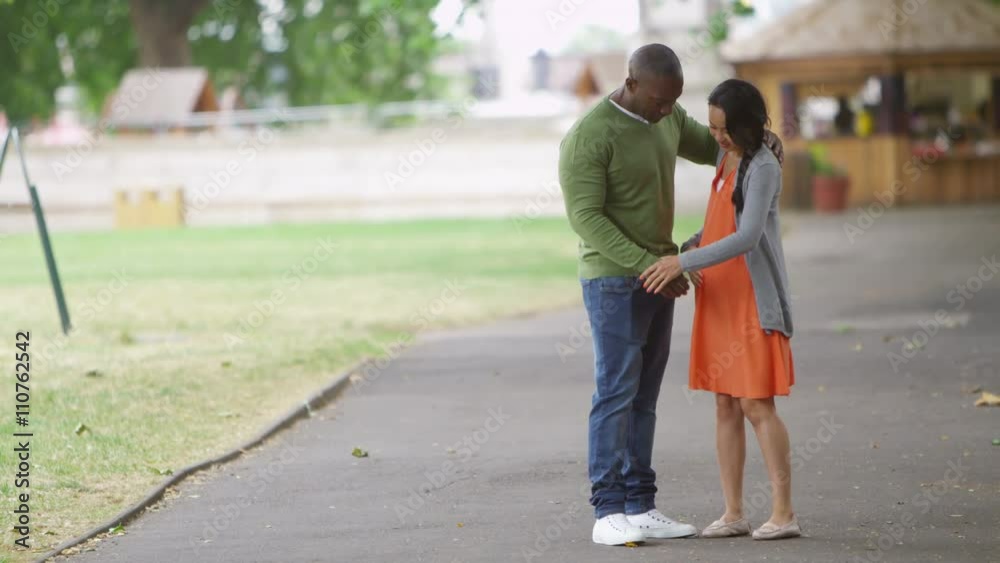 Happy mixed ethnicity couple expecting a baby going for a walk in the park Happy mixed ethnicity couple expecting a baby going for a walk in the park