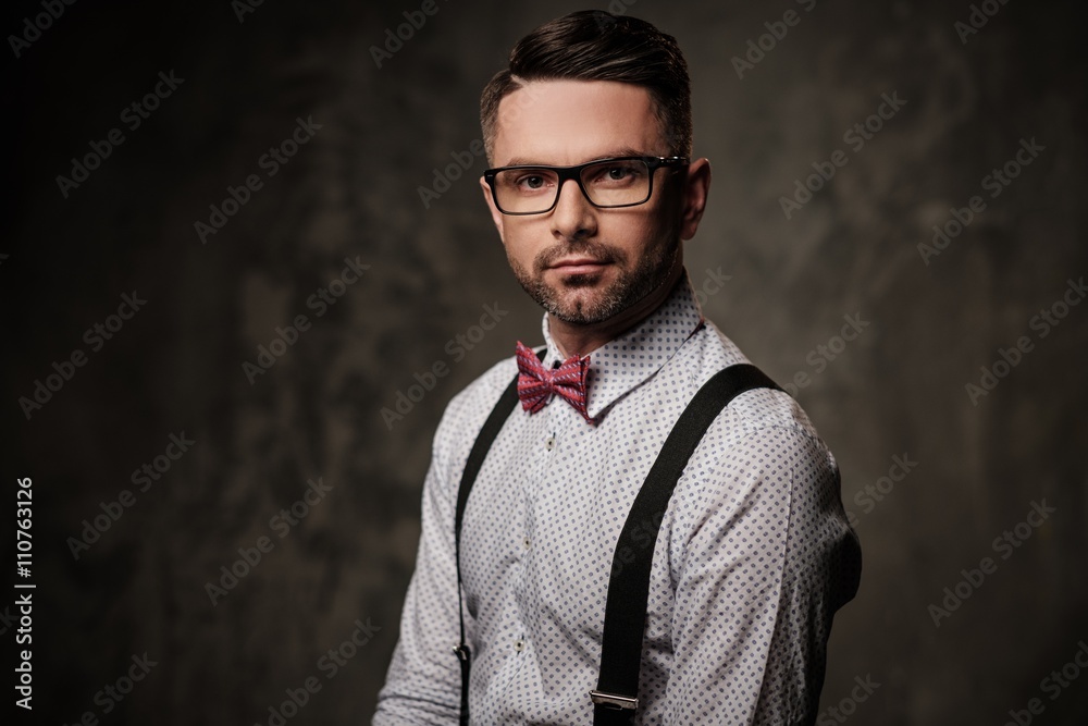 Obraz premium Stylish man with bow tie wearing suspenders and posing on dark background.