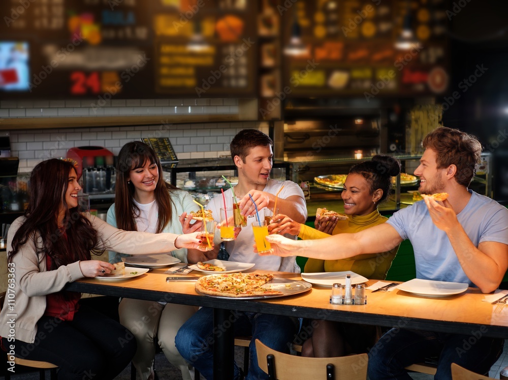 Obraz premium Cheerful multiracial friends having fun eating pizza in pizzeria.