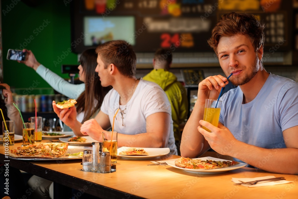 Cheerful multiracial friends having fun eating pizza in pizzeria.