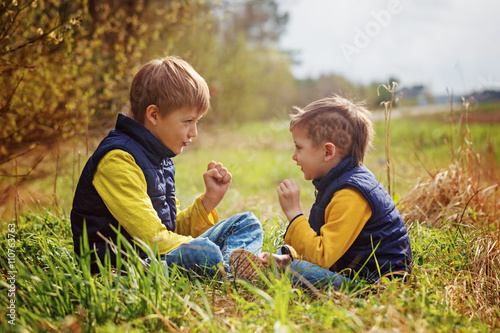 Two little brothers play in rock-paper-scissors sitting on grass