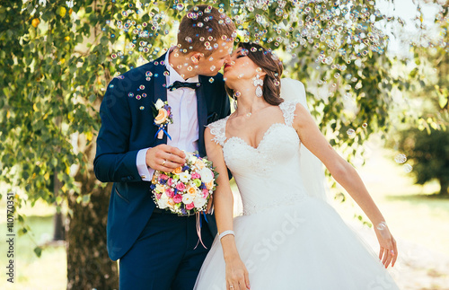 Obraz na płótnie elegant stylish groom with his happy gorgeous blonde bride have fun with soap bubble on the background of trees outdoors in park w salonie