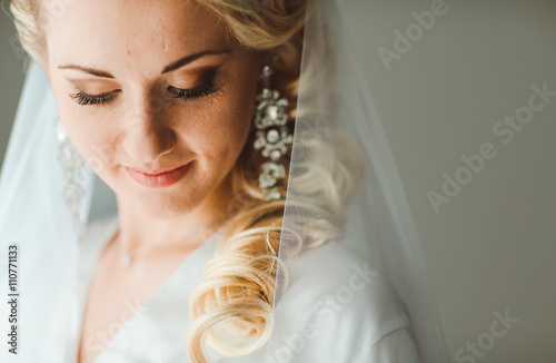 Portrait of beautiful bride with fashion veil posing at home at wedding morning. Makeup. Blondegirl with elegant hair styling. Wedding dress. Close Up photo