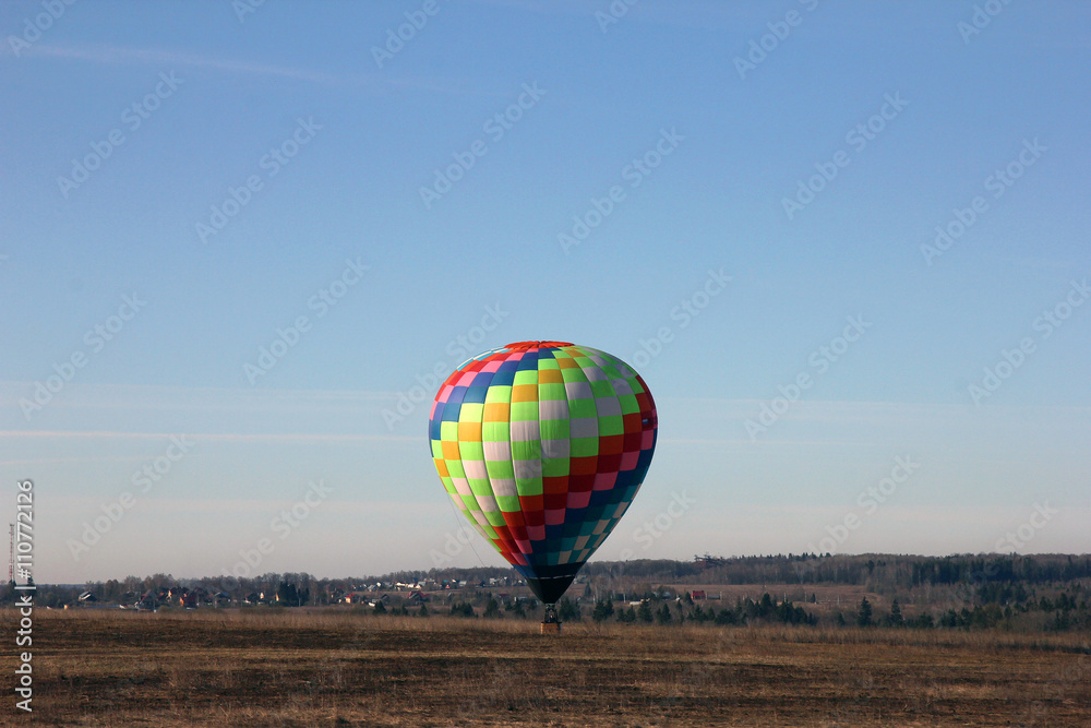 Beautiful multi-colored balloon lands in a field at the morning,