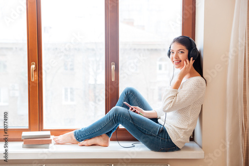 Happy woman sitting on windowsill with headphones