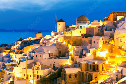 Windmills in Oia on the island Santorini, white houses and church during twilight blue hour, Greece © Kavalenkava