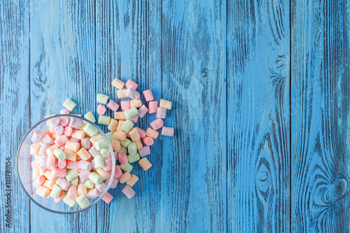 Glass bowl of colored marshmallows, on blue background