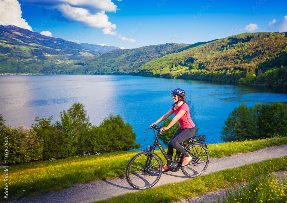 Fototapeta premium woman with e-bike cycling beside a beautiful lake-lake and bike