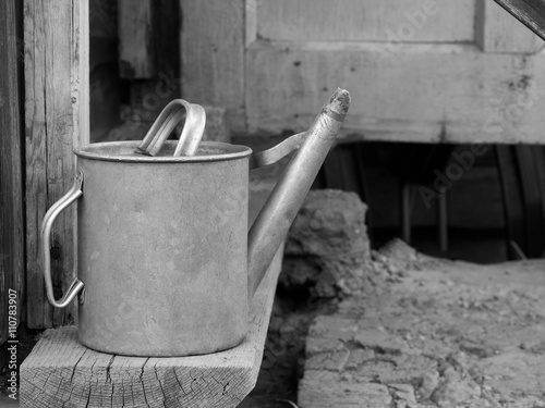 Old, dirty, metal watering can in the old walls, and the dry land.