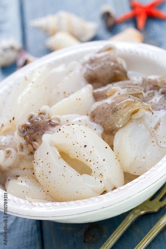 raw squids in white plate on blue background